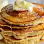 Healthy Oatmeal Apple Pancakes 10 Healthy oatmeal apple pancakes stacked on a plate, drizzled with syrup.